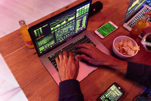 Free Hands typing on a laptop with coding, phone on desk, symbolizing cybersecurity. Stock Photo